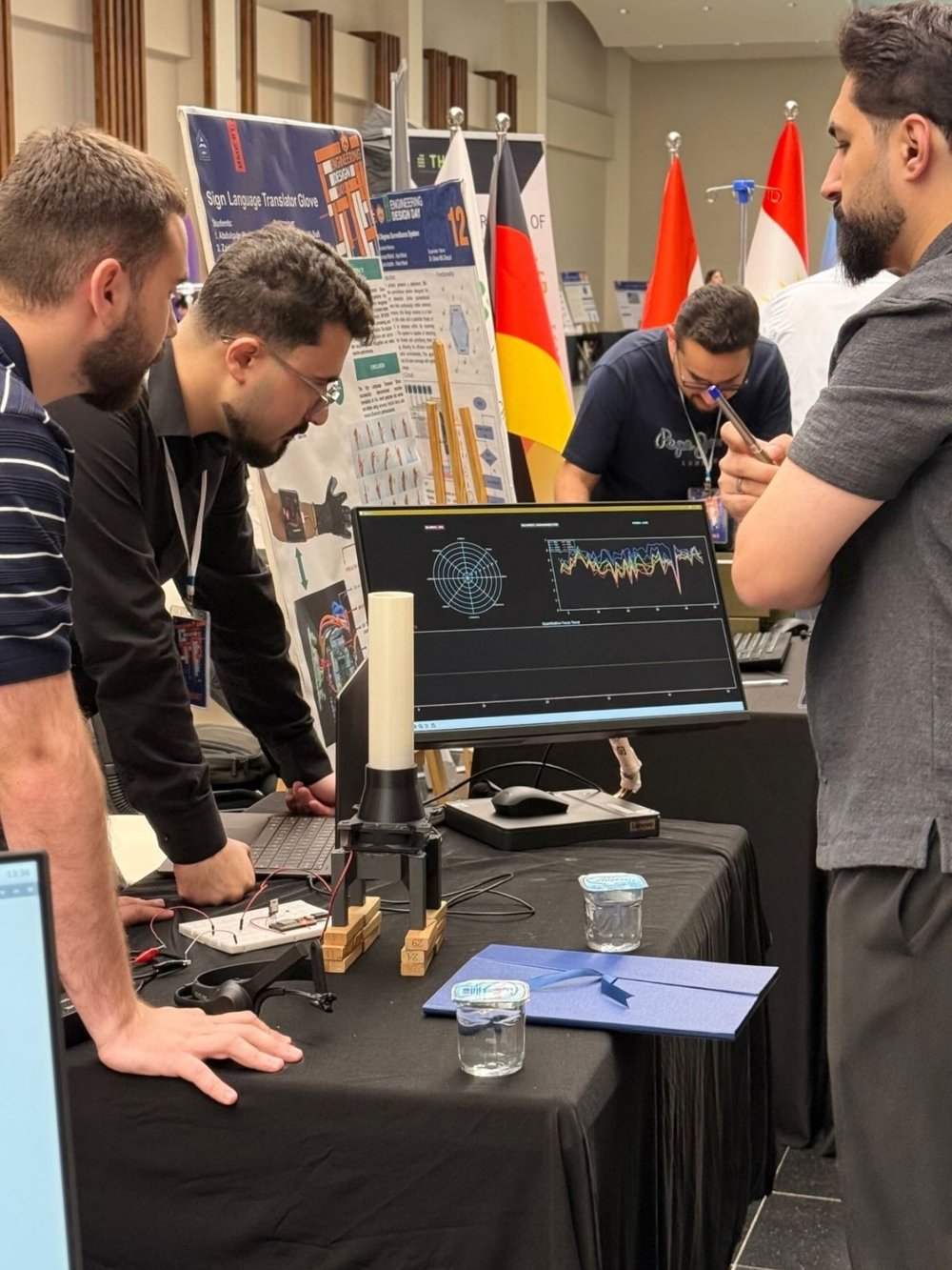 The stand in use: the tube standing on the table beside a monitor showing the live brainwave dashboard, with visitors gathered around.