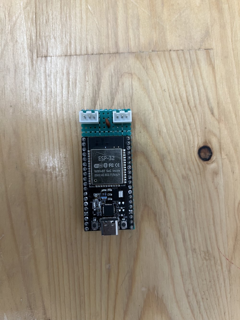 The ESP32-WROOM-32 development board with a small soldered green board sitting on top of it, carrying two white three-pin connectors.